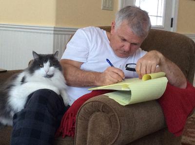 black and white cat on a mans lap while he writes in a notebook.